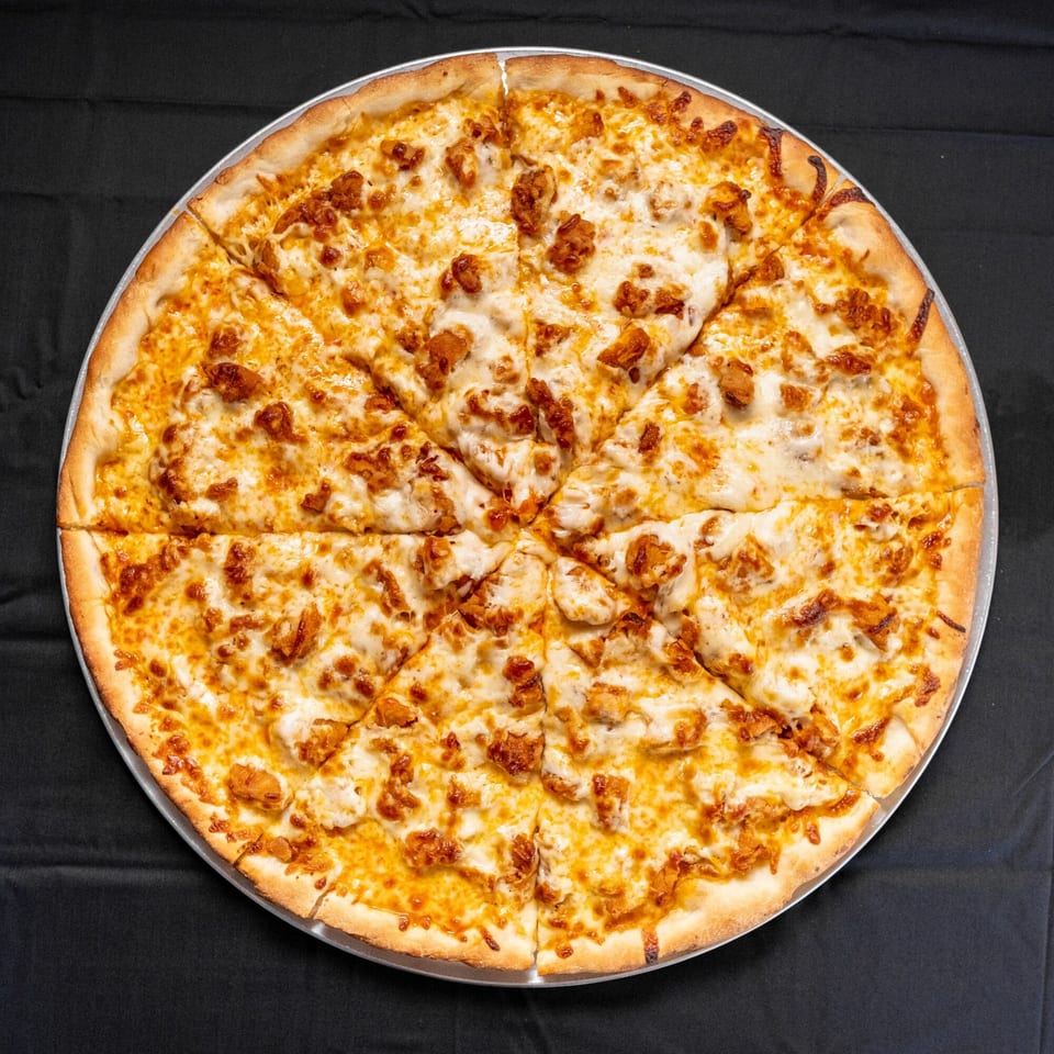 A whole D-Ray's Pizzeria buffalo chicken pizza, cut into slices, on a black tablecloth.
